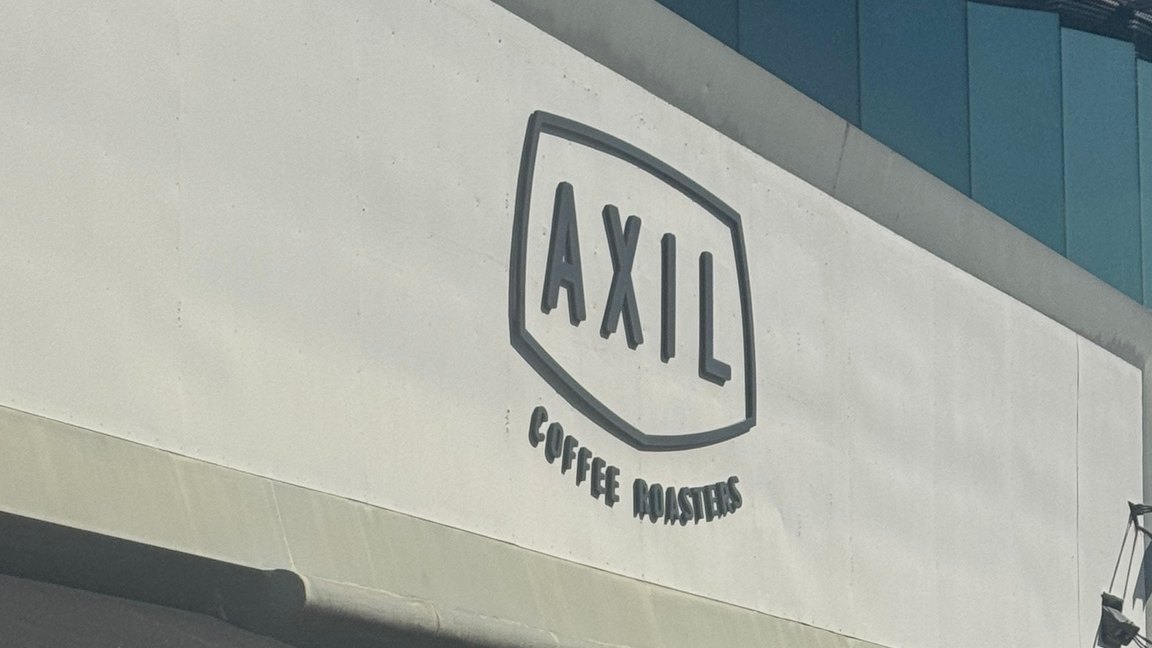 The white facade of Axil Coffee Roasters Hawthorn, with the large "AXIL COFFEE ROASTERS" logo sign and awning above the Burwood Road entrance.