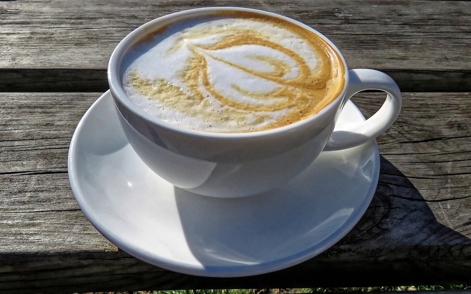 A white cup of flat white with milk foam and a brown swirl on a wooden table.