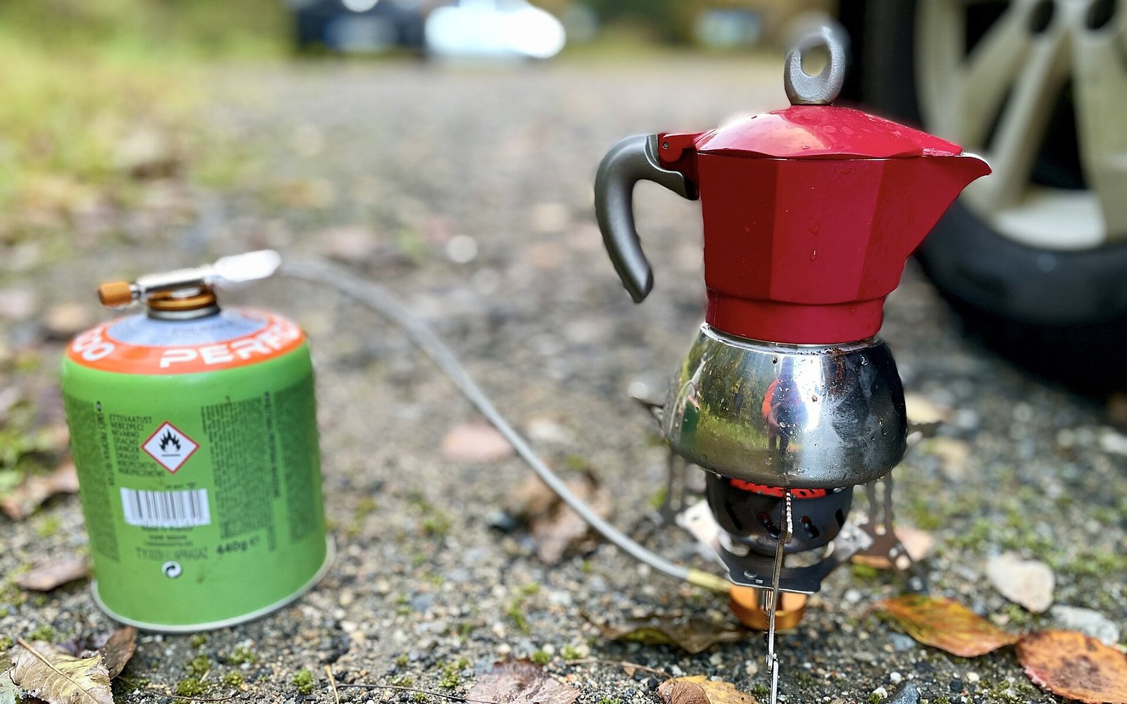 A red moka pot heating on a small gas camping stove.